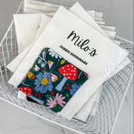 Fabric bookmark with floral design and 'milo's' branding in a wire basket.