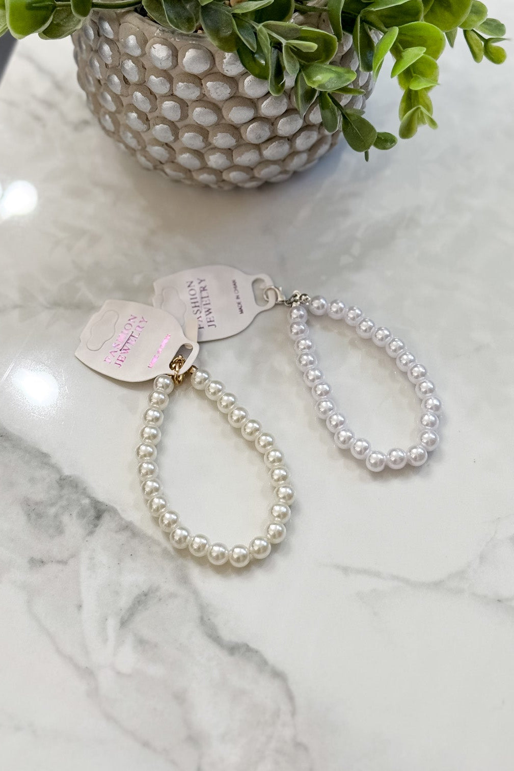 Pearl keychain on a marble surface with a small plant in the background