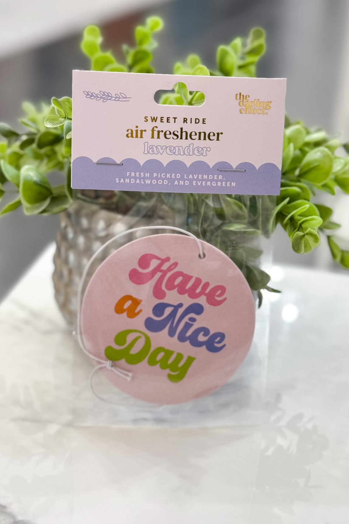 Air freshener with a plant and 'Have a Nice Day' tag on a marble surface