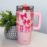 Pink tumbler with bow pattern on a white surface with a plant in the background