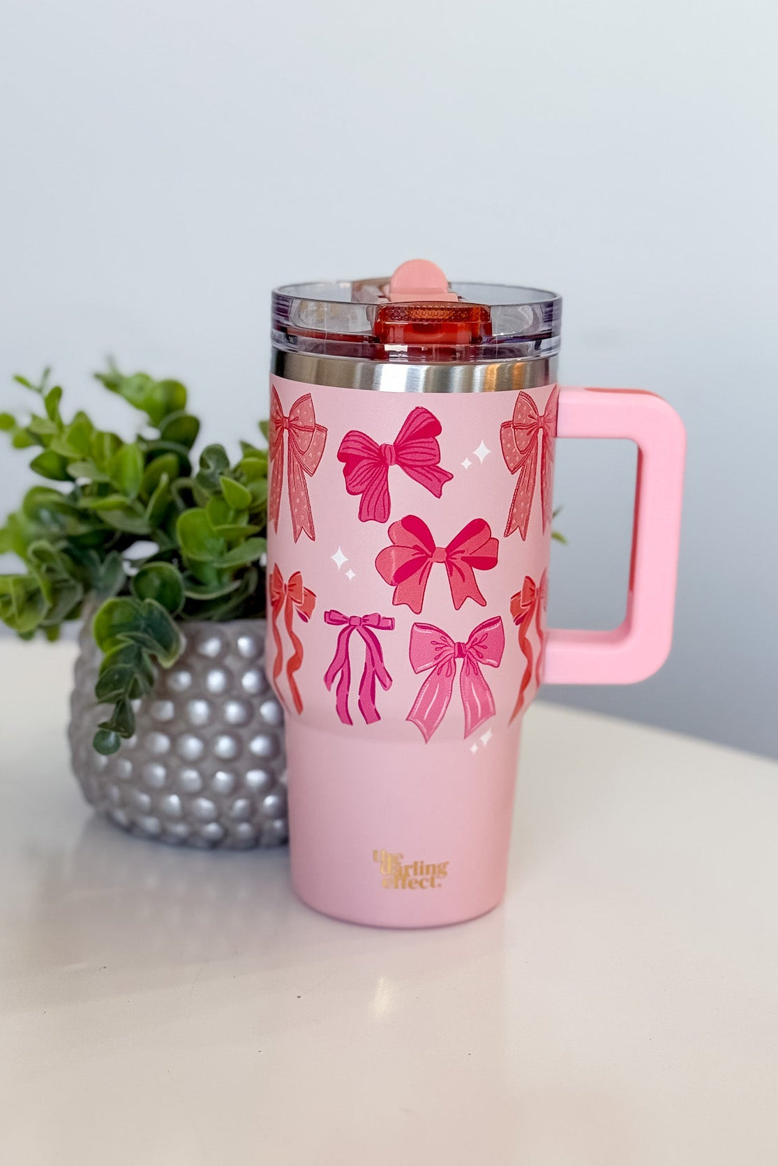 Pink tumbler with bow pattern on a white surface with a plant in the background