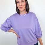 Woman wearing a purple sweater and jeans against a white wall