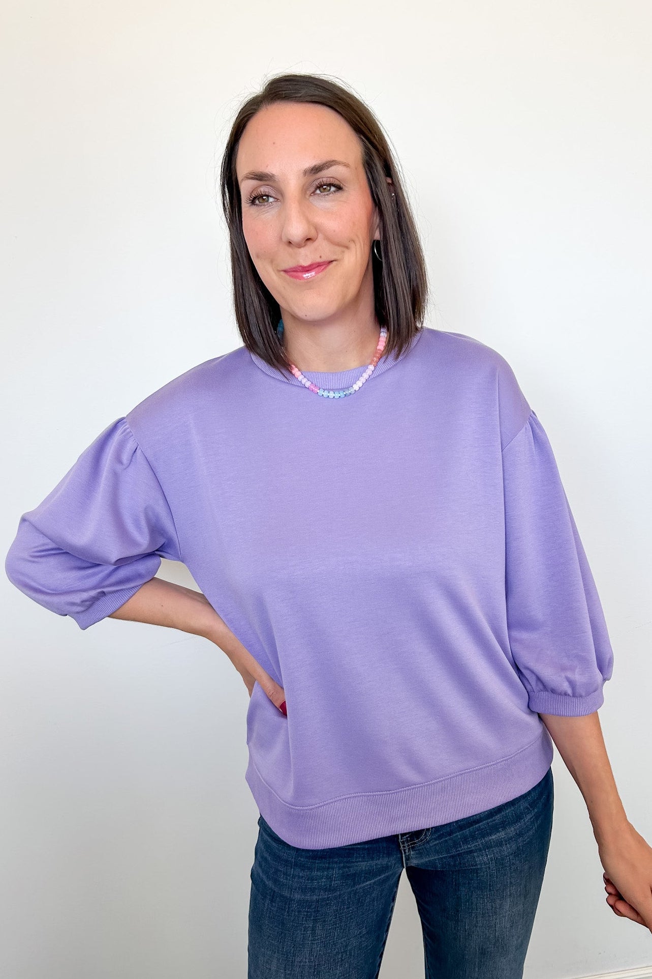 Woman wearing a purple sweater and jeans against a white wall