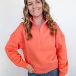 Woman wearing a bright orange pullover with a quarter zip against a white background