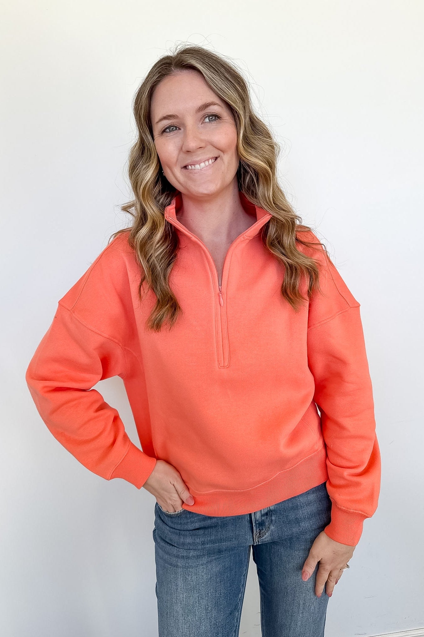 Woman wearing a bright orange pullover with a quarter zip against a white background