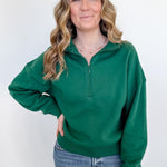 Woman wearing a green pullover with a quarter zip on a white background