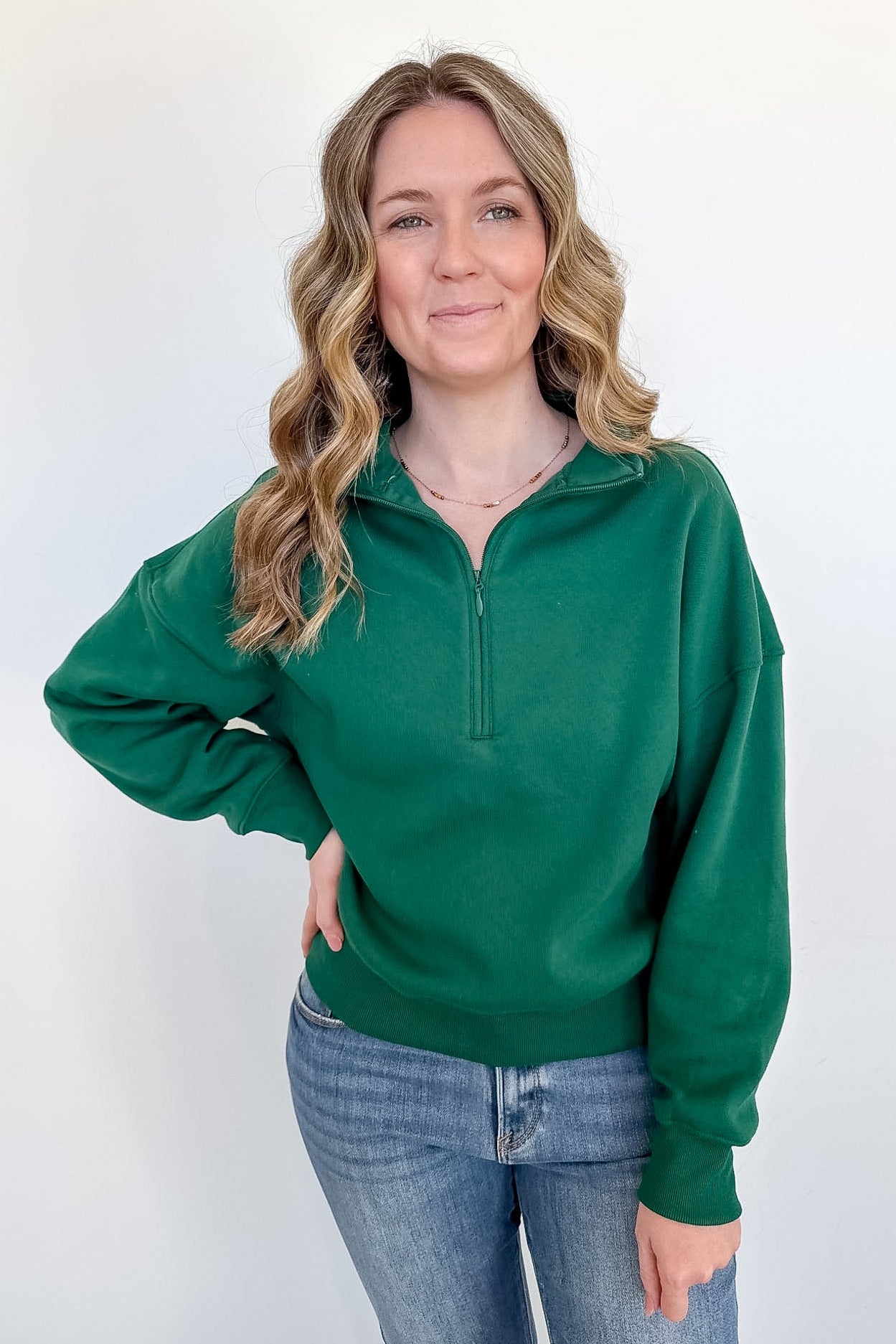 Woman wearing a green pullover with a quarter zip on a white background
