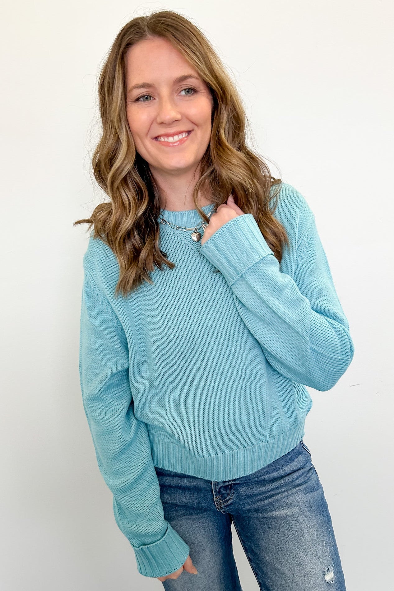 Woman wearing a light blue sweater and jeans against a white background