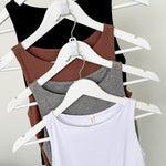 Four tank tops in black, brown, gray, and white on hangers against a plain background