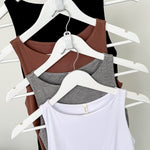 Four tank tops in black, brown, gray, and white on hangers against a plain background