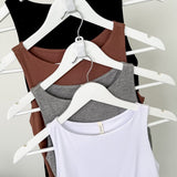 Four tank tops in black, brown, gray, and white on hangers against a plain background
