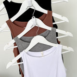 Four tank tops in black, brown, gray, and white on hangers against a plain background
