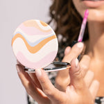 Woman applying makeup with a compact mirror and pink lip balm.