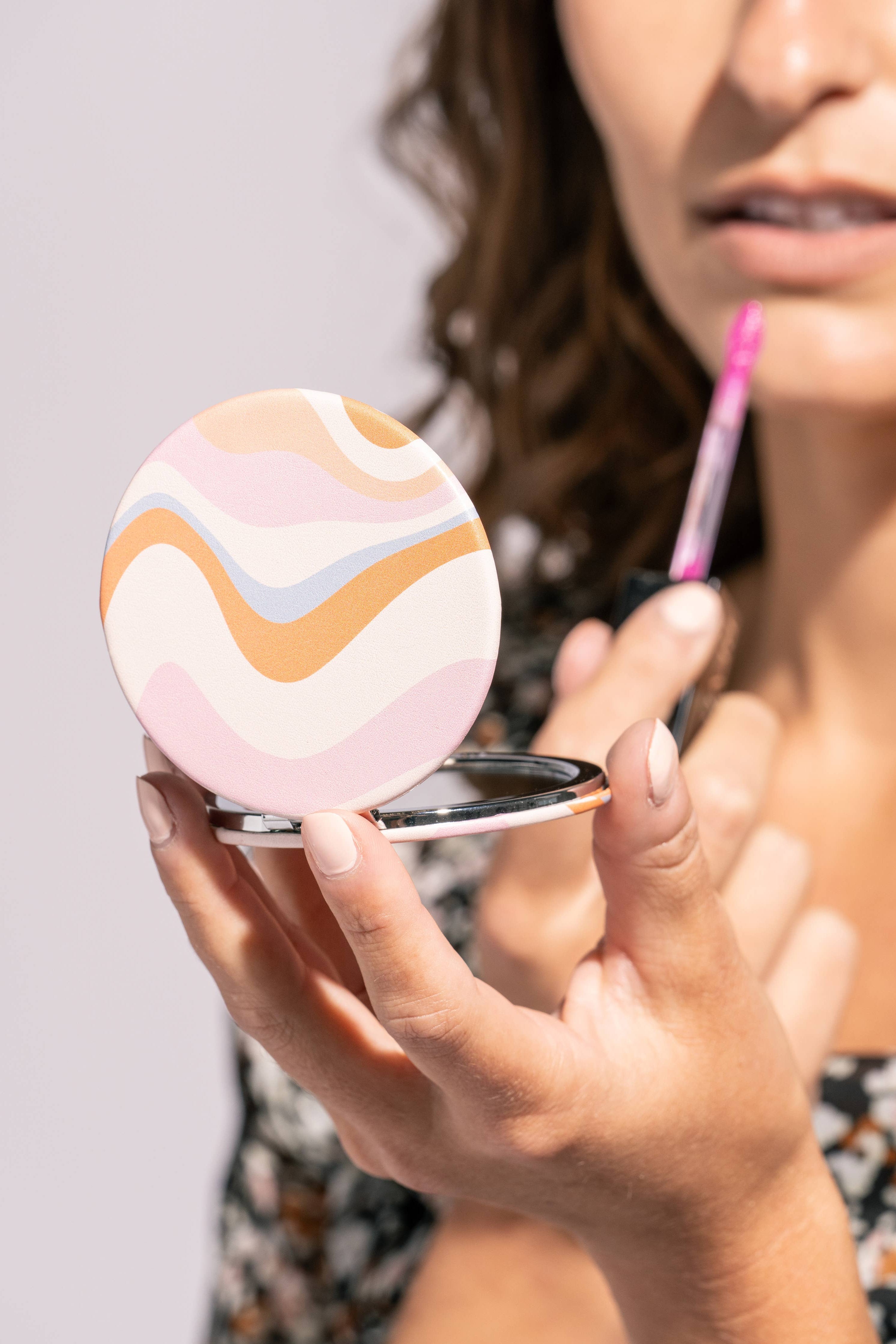 Woman applying makeup with a compact mirror and pink lip balm.
