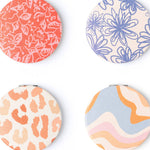 Four round coasters with floral, abstract, and animal print designs on a white background.