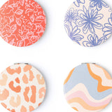Four round coasters with floral, abstract, and animal print designs on a white background.