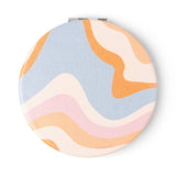 Round compact mirror with pastel wave pattern on a white background