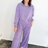 Woman wearing a purple tracksuit standing against a white wall.