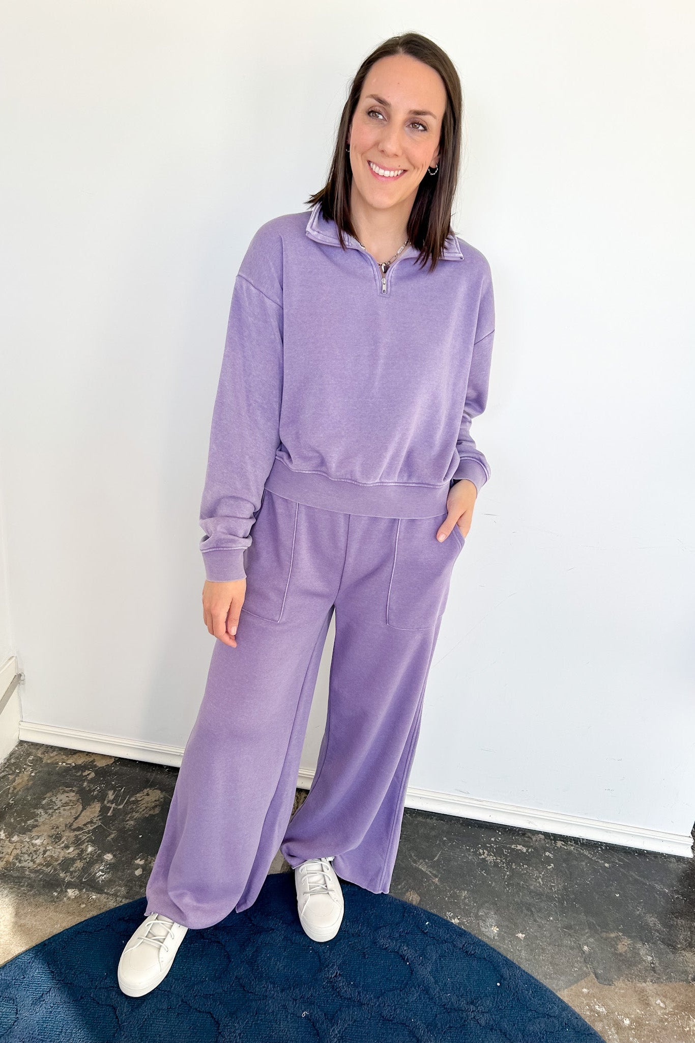 Woman wearing a purple tracksuit standing against a white wall.