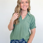 Woman wearing a green top and blue floral pants against a white background