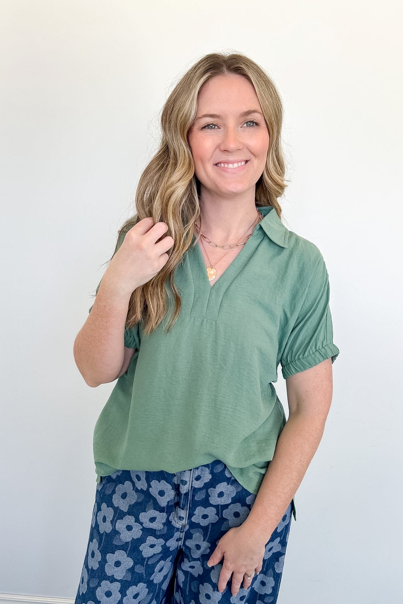 Woman wearing a green top and blue floral pants against a white background