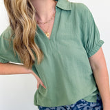 Woman wearing a green top and blue floral pants against a white background