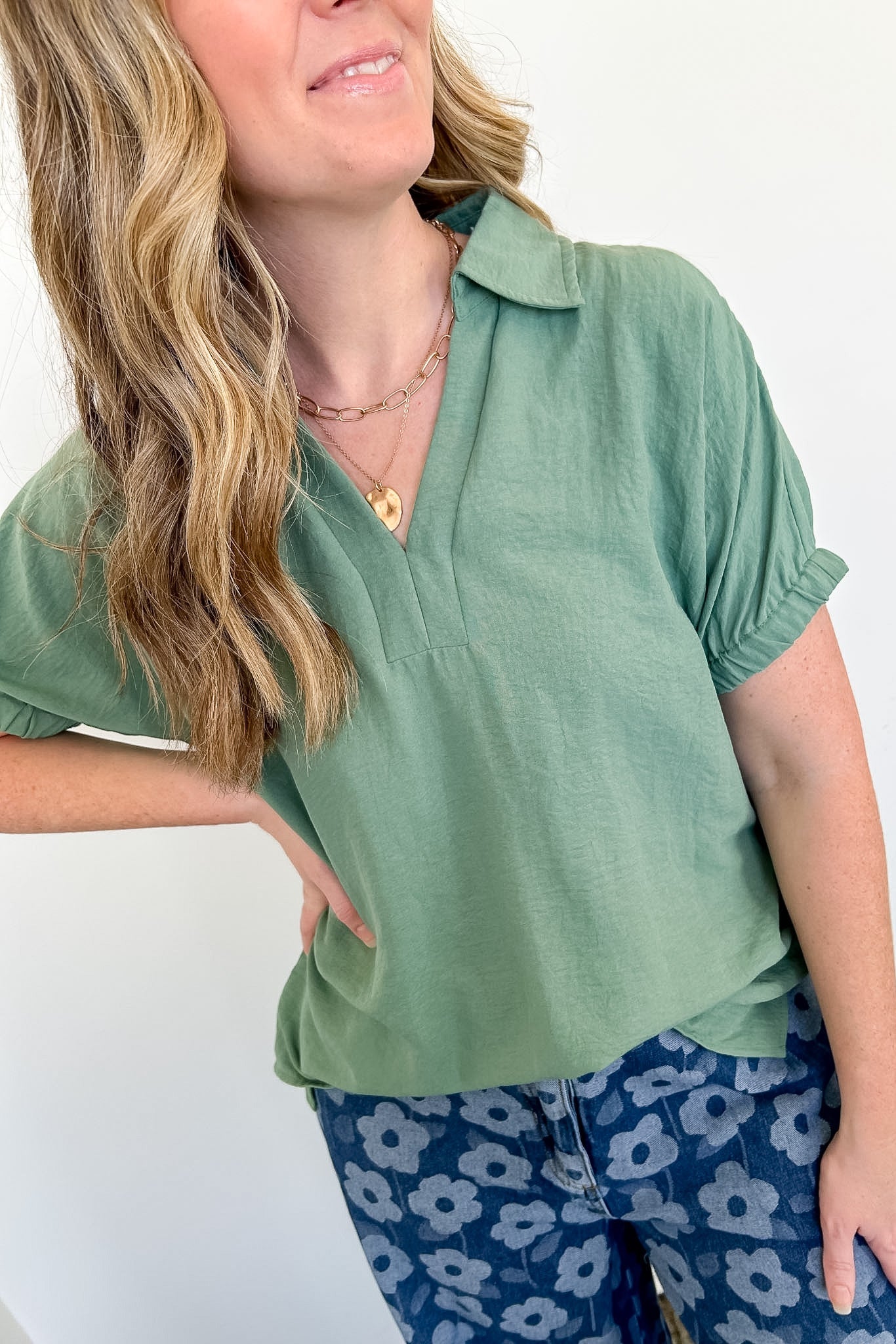 Woman wearing a green top and blue floral pants against a white background