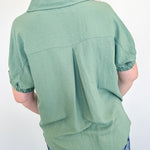 Person wearing a green shirt and blue floral pants against a white wall.