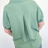 Person wearing a green shirt and blue floral pants against a white wall.