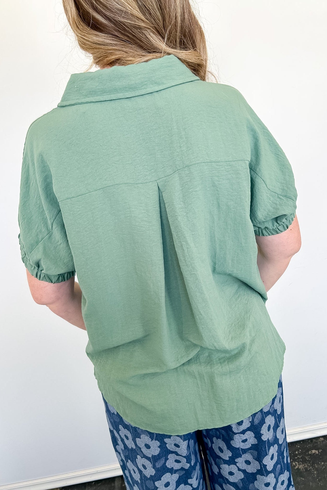 Person wearing a green shirt and blue floral pants against a white wall.