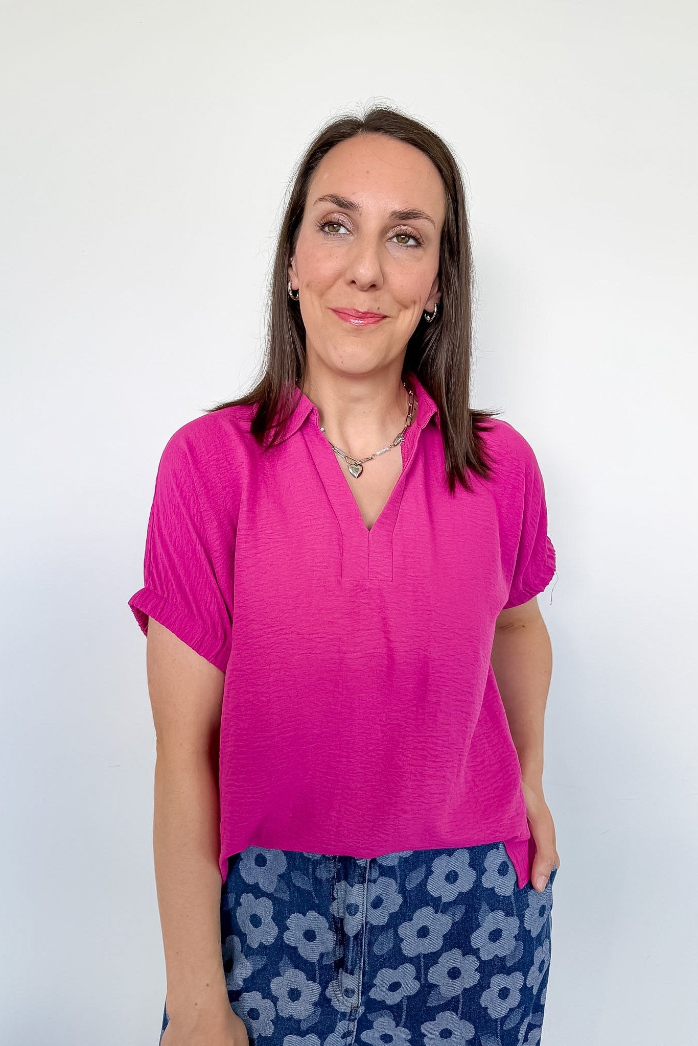 Woman wearing a pink shirt and floral pants against a white background
