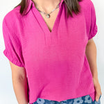 Woman wearing collared pink shirt with a silver necklace.