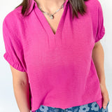 Woman wearing collared pink shirt with a silver necklace.