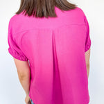 Person wearing a bright pink top and blue patterned pants against a white wall.