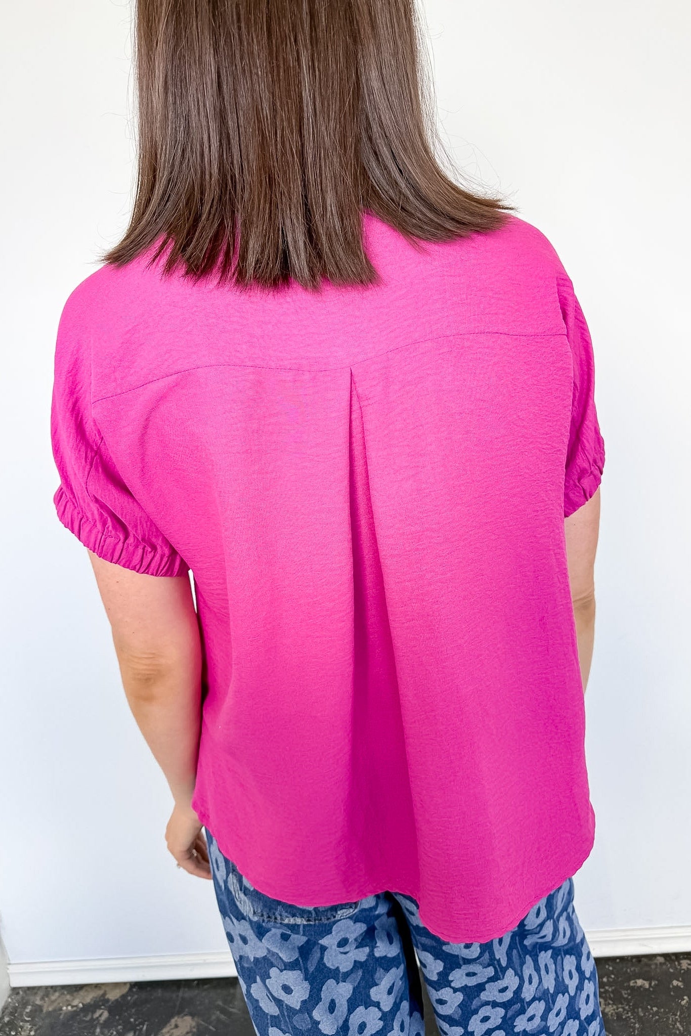 Person wearing a bright pink top and blue patterned pants against a white wall.
