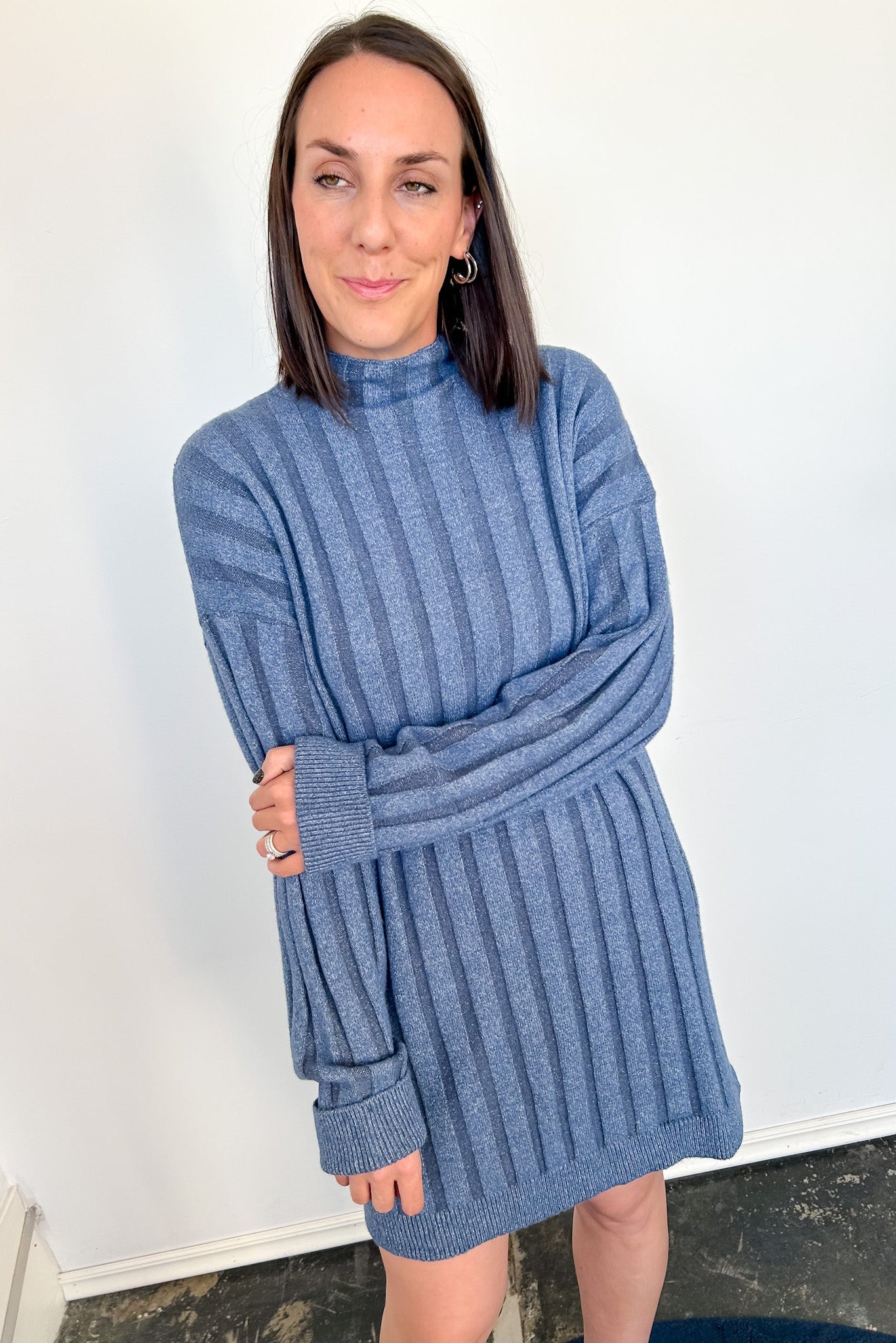 Woman wearing a blue ribbed sweater dress against a white wall.