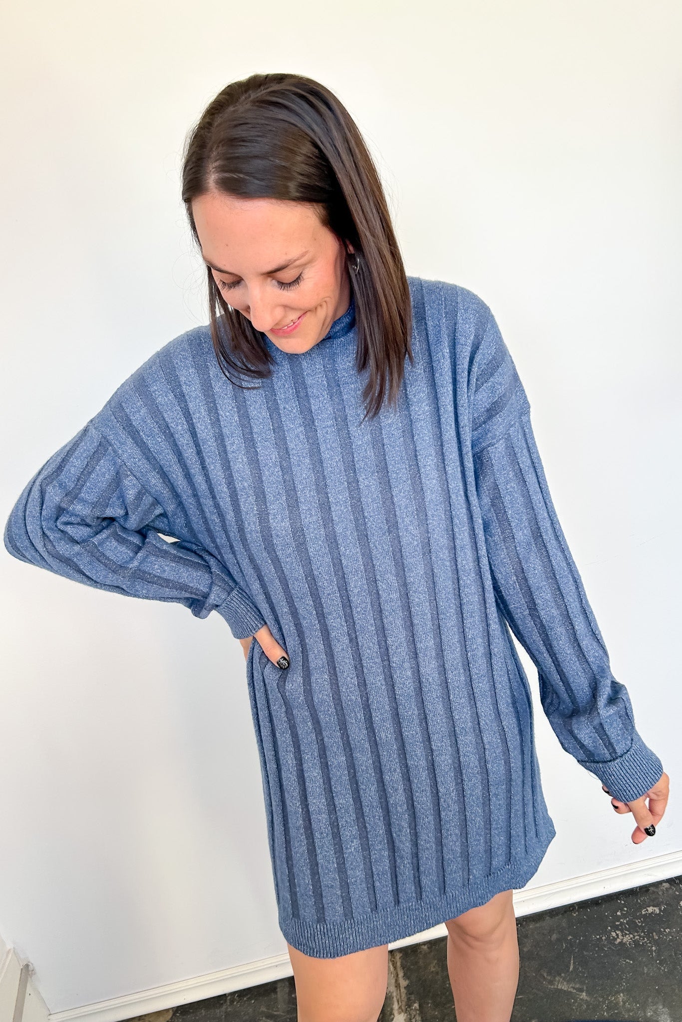 Woman wearing a short blue sweater dress against a white wall.
