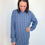 Woman wearing a blue ribbed sweater dress against a white wall