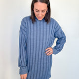 Woman wearing a blue ribbed sweater dress against a white wall