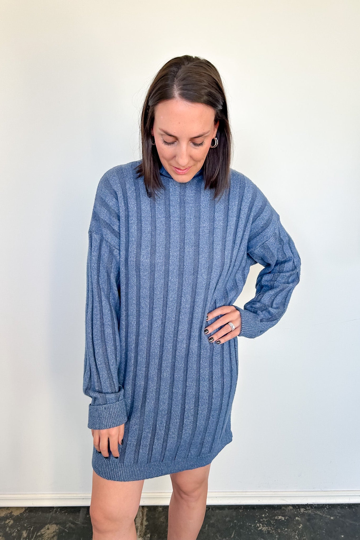 Woman wearing a blue ribbed sweater dress against a white wall