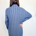 Person wearing a blue ribbed sweater against a white wall