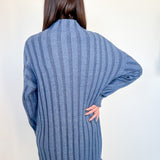 Person wearing a blue ribbed sweater against a white wall