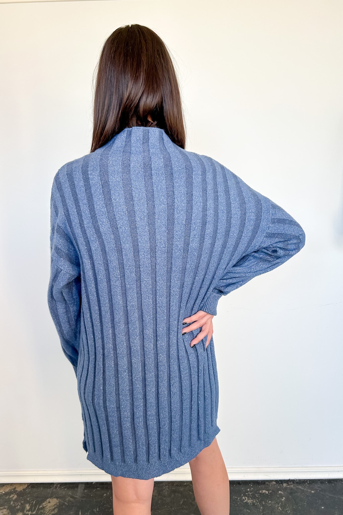 Person wearing a blue ribbed sweater against a white wall
