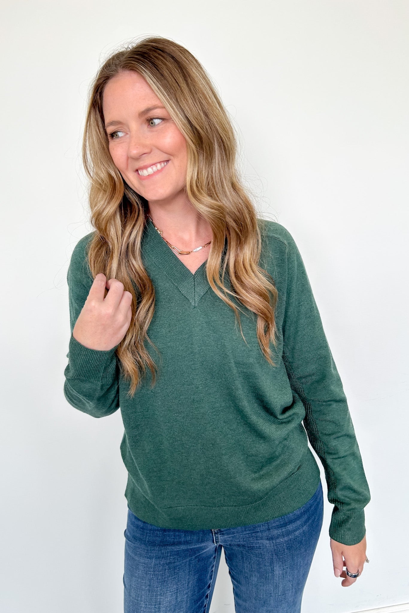 Woman wearing a green sweater and blue jeans against a white background