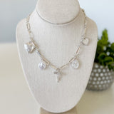 Silver necklace with charms on a white bust against a light background