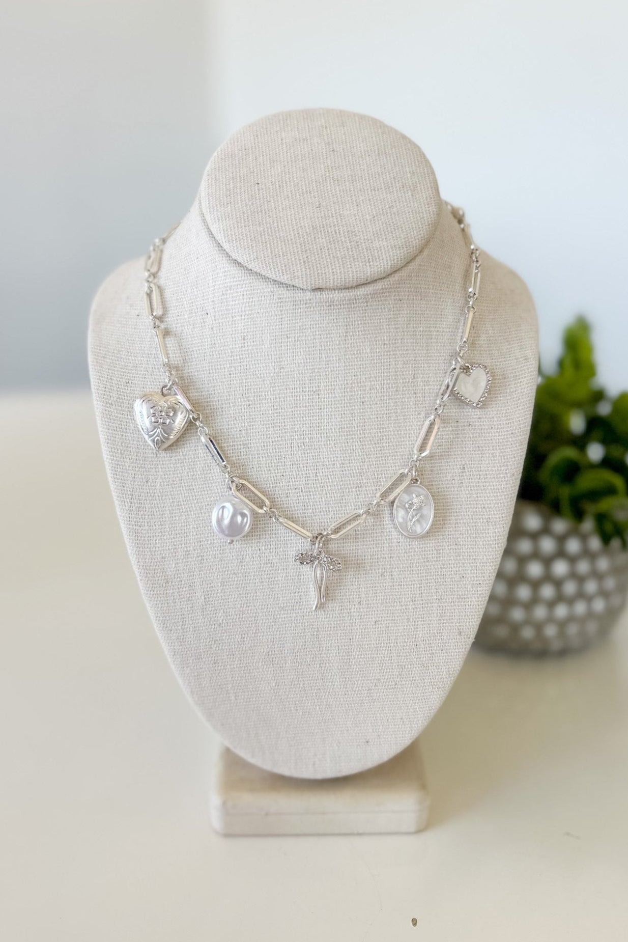Silver necklace with charms on a white bust against a light background