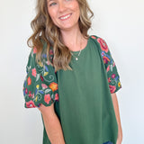 Woman wearing a green top with floral sleeves against a white background