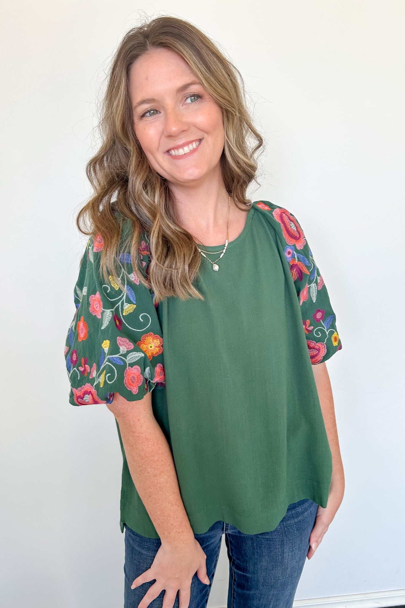 Woman wearing a green top with floral sleeves against a white background