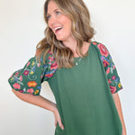 Woman wearing a green top with floral sleeves against a white background