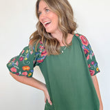 Woman wearing a green top with floral sleeves against a white background